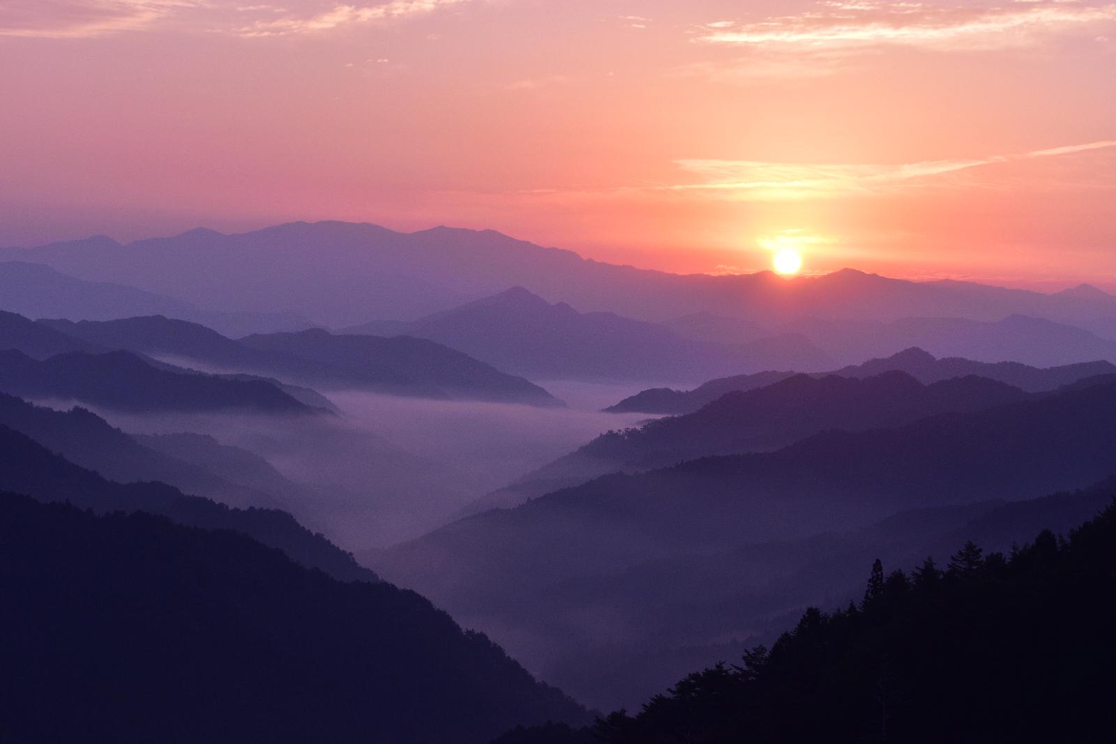 オレンジ色に光る夕暮れの太陽と山にかかる雲海の写真