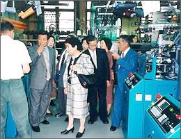青い機械などが置いてある工場の中で説明を受けながら見学をする訪問団の写真