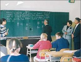 訪問団の一人が子供たちを前に黒板に「男女」「平和」「日本」などの日本語を書いている写真