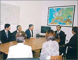 世界地図が壁に貼られている部屋で説明を聞く訪問団の写真